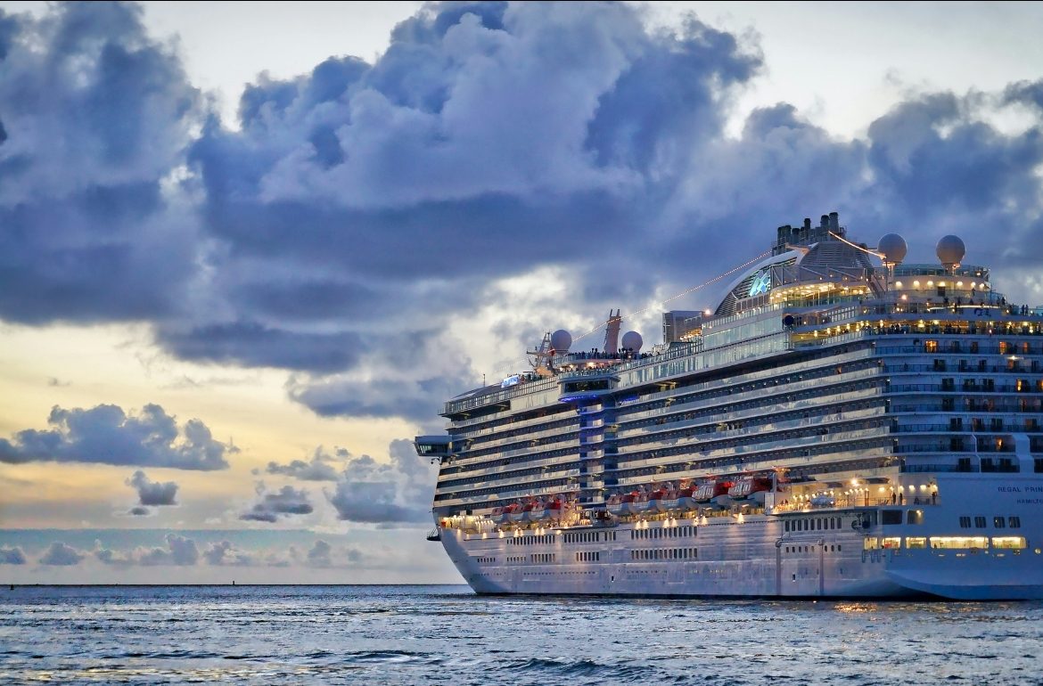 A cruise ship sailing at dusk under a pink and purple sky